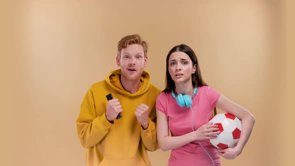 Young Couple Man and Woman Happy with a Soccer Ball Cheering for a Football Match on a Beige