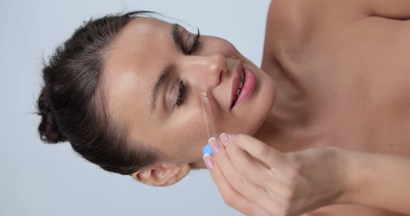 Close Up Vertical Portrait of Young Woman Applying Serum on Her Cheek Skin Care Gray Studio