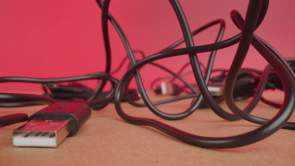 Tangled Wires of USB Cables Lie on Table on Pink Background