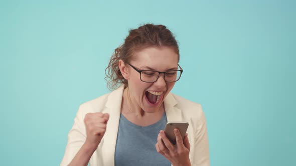 Happy Woman with Glasses Uses Phone and Emotionally Rejoices in the Studio