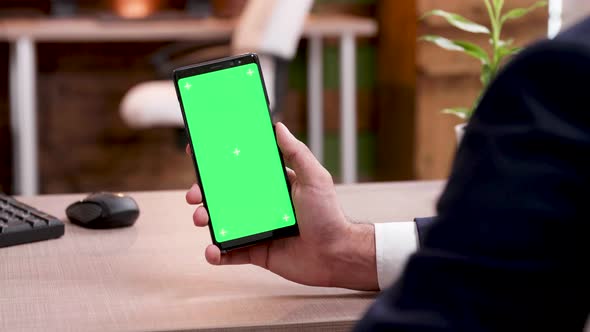 Rear View of Businessman in His Office Holding Mobile Phone with Green Screen