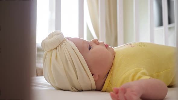 Playful Baby Girl in Yellow Clothes Lies in Bassinet Closeup