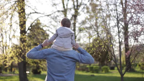 Adorable Little Daughter Sitting on Dad's Neck and Laughing. Young Father Walk with His Cute