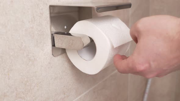 Men's Hands Unwind and Tear Off a Short Piece of Toilet Paper