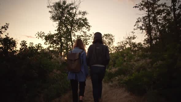 View From Back Two Modern Women Walking Through Forest During Sunset with Amazing Sky Slow Motion