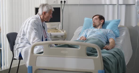 Hospitalized Man Lying in Bed Talking to Senior Doctor