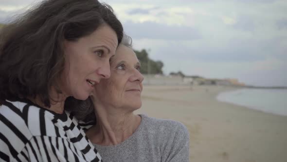 Happy Adult Daughter Hugging Senior Mother and Looking at Ocean