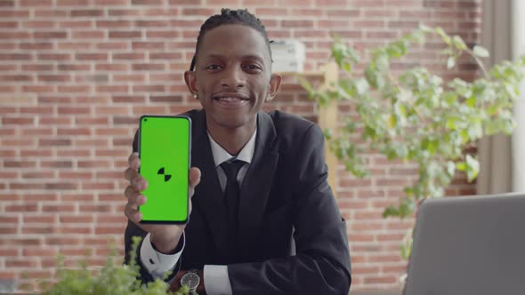 Black man businessman in an official suit sits at a desk in office and smiles shows the green screen