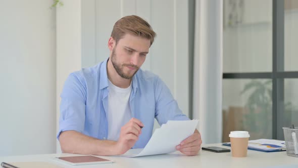 Young Creative Man Reading Documents in Office