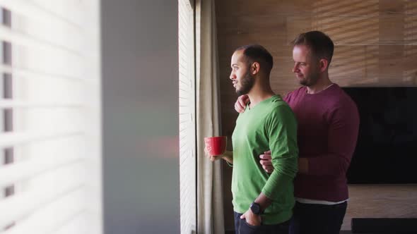 Multi ethnic gay male couple drinking coffee and embracing