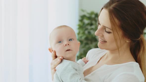 A Young Mother Holds a Newborn Baby in Her Arms While the Baby Looks at the Camera