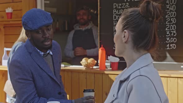 Serious African American man listen to brunette Caucasian girl's speech near coffee-shop