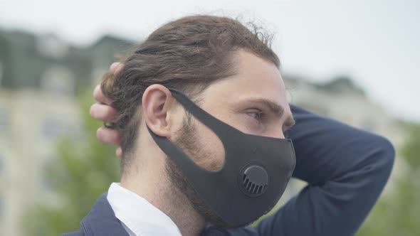 Close-up Side View of Young Caucasian Businessman in Covid-19 Face Mask Standing Outdoors