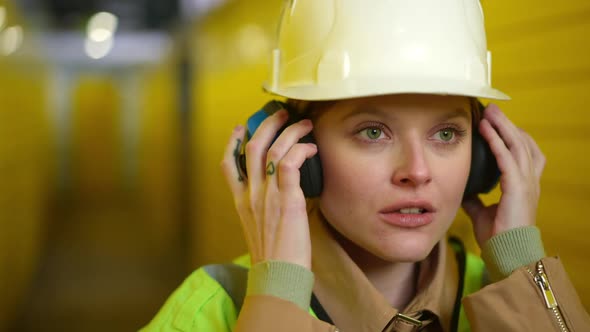 Closeup Beautiful Young Woman with Green Eyes in Hard Hat Putting on Headphones on Break Standing in
