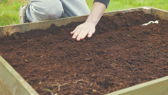 Placing soil over sown vegetable seeds in raised garden bed