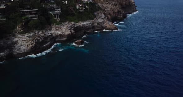 Drone shot of a cliffside beach that has both amazing houses and a nice views of the waves crashing