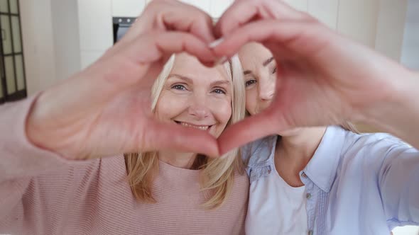 Happy Smiling Senior Woman Mother and Her Grown Up Daughter Make Heart Shape Hand Gesture Sitting on