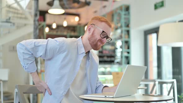 Redhead Man with Back Pain Using Laptop in Cafe