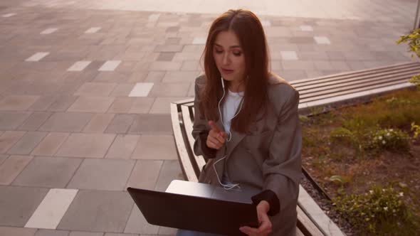 Young attractive business woman sitting outdoor on the bench using laptop