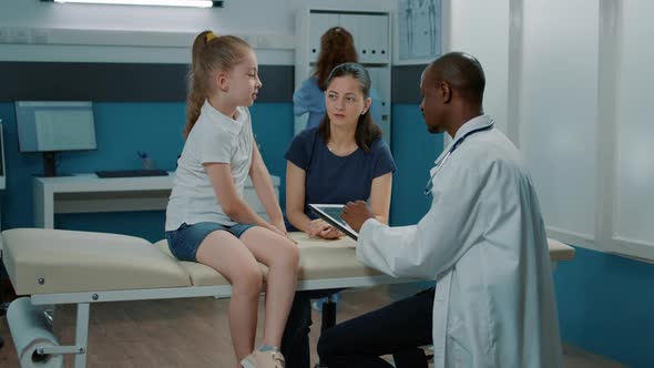 African American Medic Taking Notes on Digital Tablet to Consult Kid