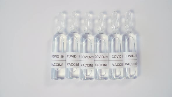 row of medical glass ampoules with a vaccine from COVID-19 on a wooden surface.