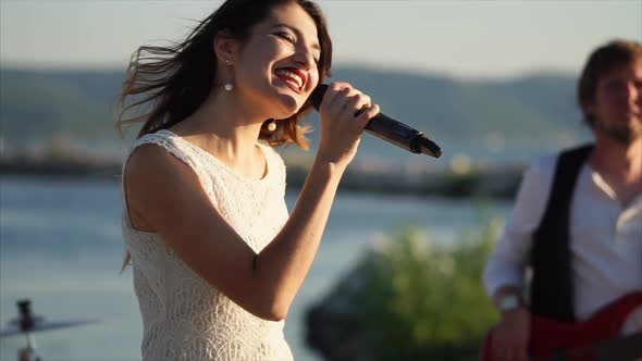 A Young and Pretty Girl Sings an Energetic Song Into an Outdoor Microphone