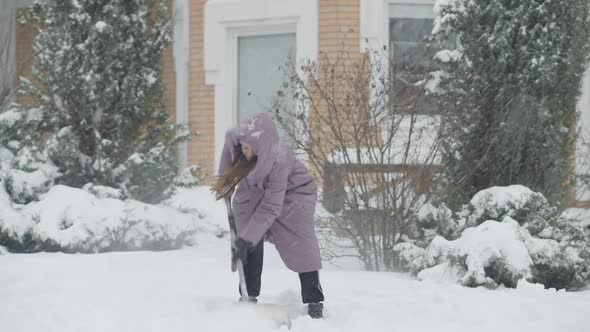 Wide Shot Portrait of Slim Beautiful Young Woman Cleaning Snow on Backyard in Winter