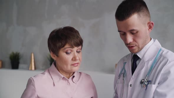 Attractive Senior Woman and Serious Young Caucasian Doctor Are Talking About Diagnosis.