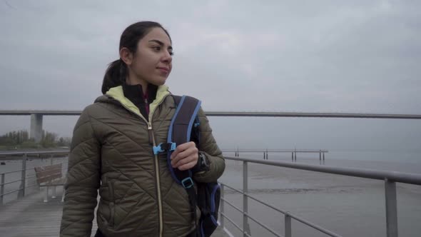 Happy Brunette Hindu Woman with Backpack Walking on Wooden Jetty