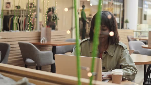 Middle-aged African Woman Using Laptop in Cafe