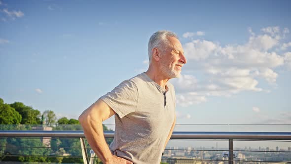 Cheerful Senior Man Does Pelvic Rotation on Observation Deck