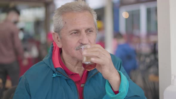 Close up of caucasian old man look far away and drink Turkish tea in the restaurant.