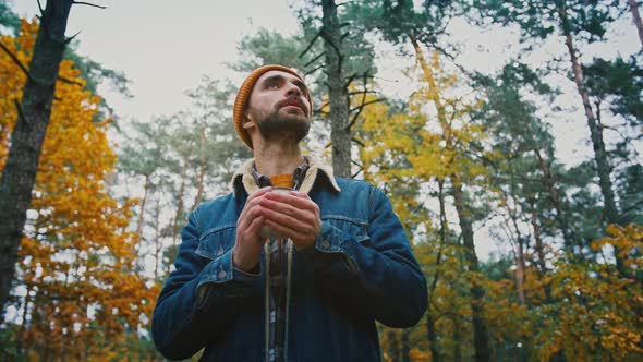 Tracking Shot of Male Traveler Watching Calm Autumn Nature in Forest Warming Hands of Tea Mug Below