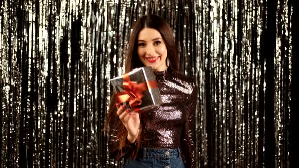 a Girl in a Shiny Jacket and Skirt with a Gift on a Silver Background in the Form of Rain