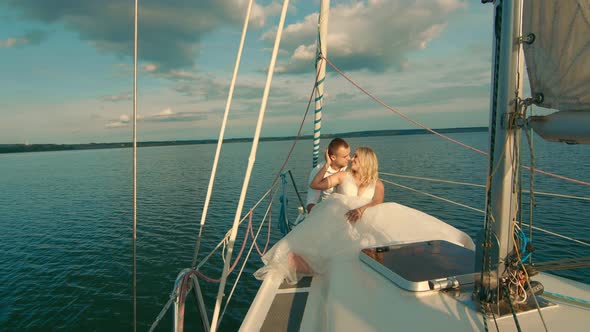 Brides Sit on a Yacht, Looking at Each Other. Beautiful Landscape Behind Them. The Bride Smiles