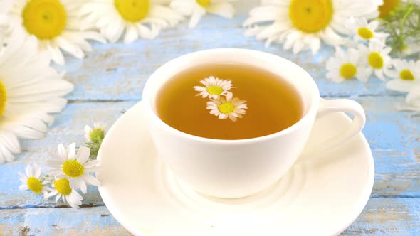 Composition with chamomile flowers and white cup of herbal tea