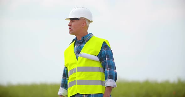 Engineer with Blueprint Analyzing Farm Against Sky