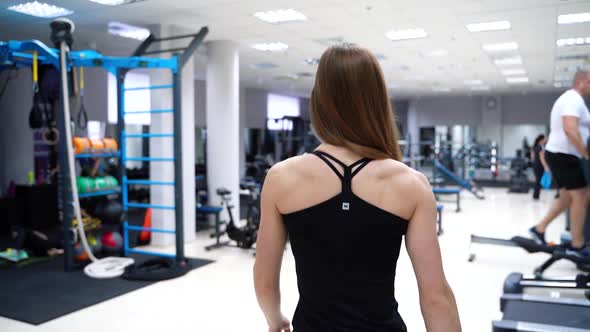 Athletic woman with her back is going to the simulator in the gym