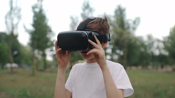 Happy Boy in Virtual Reality Glasses Plays Video Games Outdoors