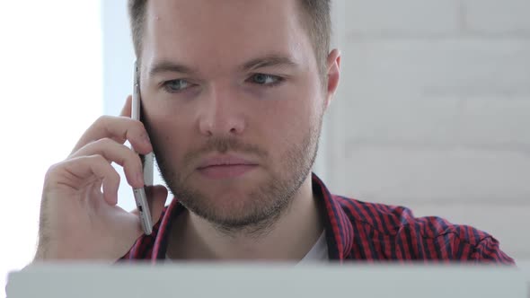 Young Man Talking on Phone While Working On Laptop