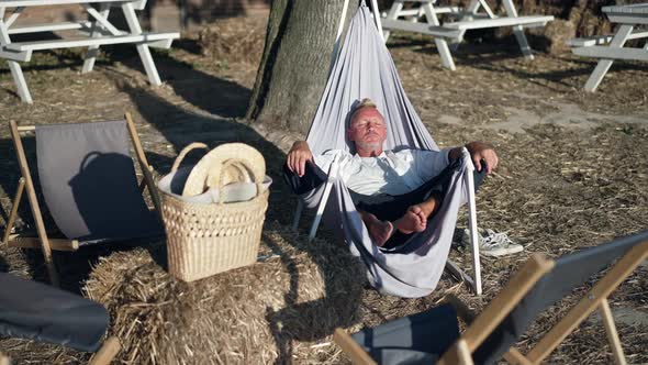 Wide Shot Relaxed Caucasian Man in Sunshine in Fabric Garden Chair Enjoying Leisure on Eco Resort