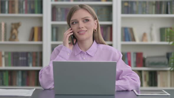 Woman Talking on Phone While Using Laptop in Office