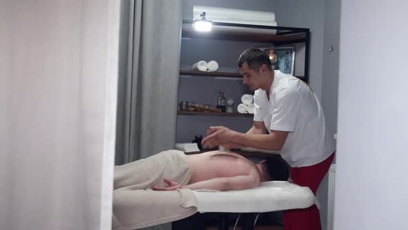 Masseur in Uniform Massaging Man's Neck in Massage Room