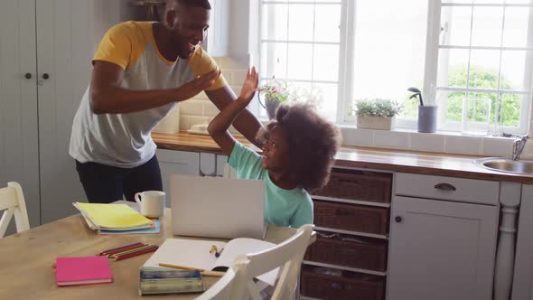 African american daughter and her father using laptop together at kitchen table