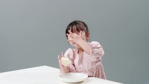 Happy little Asian girl rub her eyes, smile and enjoy eaing crispy butter toast at home.