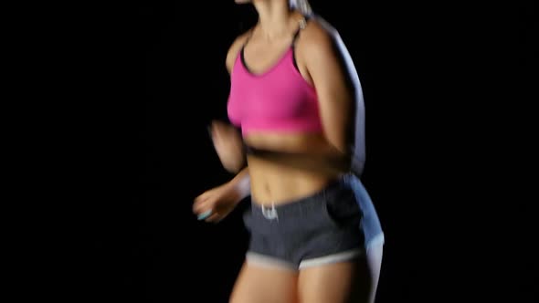 Girl Sporty in Shorts with Pockets Running on a Black Background. Close Up