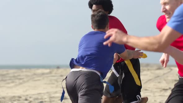 A group of guys playing flag football on the beach.