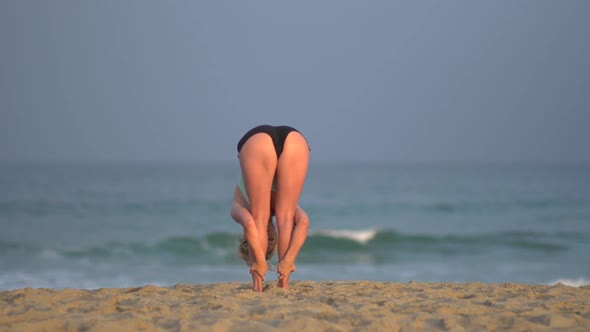 The back of a young woman doing yoga on the beach.