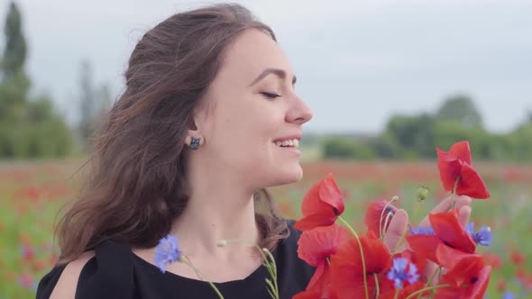 Portrait of a Pretty Girl in a Poppy Field Sniffing Bouquet of Flowers