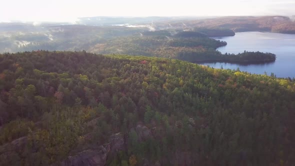 Aerial Daytime Wide Shot Flying Over Fall Forest Colors Toward Calm Misty Lakes Panning Right To Rev